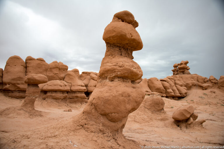 A tall sandstone pedestal with stacked rounded caps stands among smaller hoodoos.