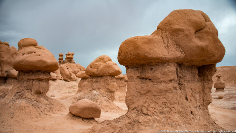 A double-lobed sandstone capstone tops a grooved column among smaller hoodoos in the basin.