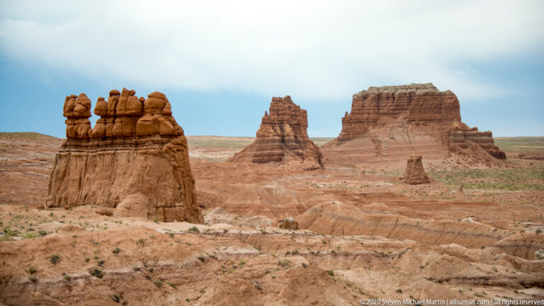 A capped hoodoo, a distant tower, and a flat-topped mesa rise across an open basin.