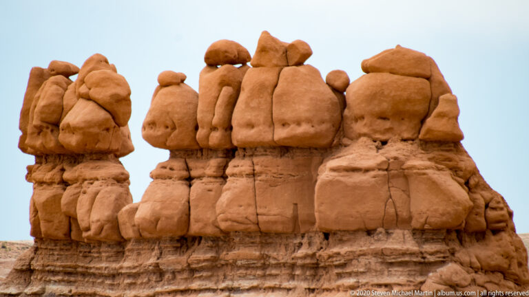 Rounded sandstone caps line a layered rock wall beneath a narrow strip of sky.