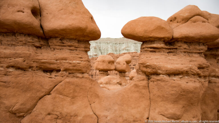 Large hoodoos frame smaller formations and a pale distant cliff through a narrow opening.