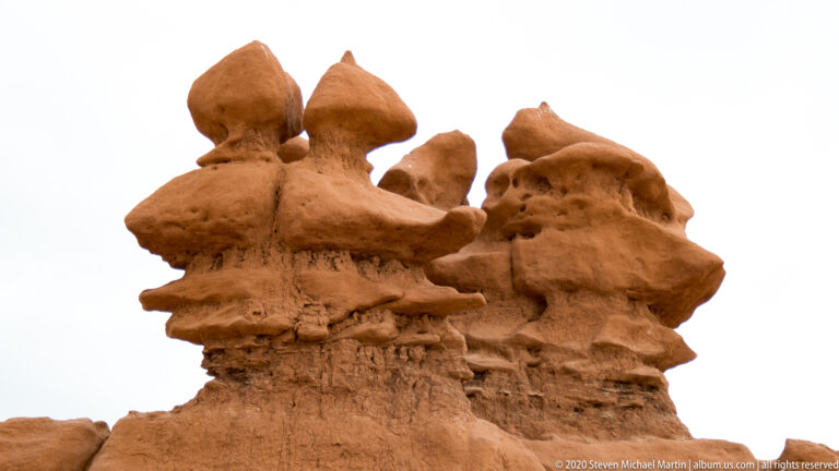 A rounded sandstone tower rises beside a larger hoodoo beneath a gray clouded sky.