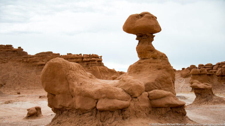 A rounded capstone tops a narrow pedestal rising from a low sandstone platform.