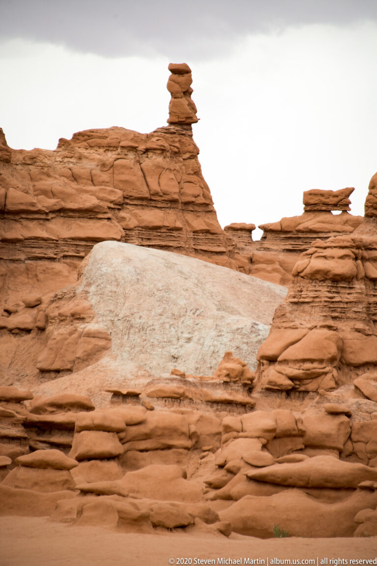 A slender stack of flat rock slabs stands on a layered sandstone ridge.