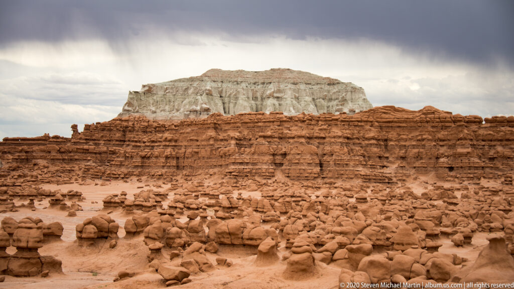 Rounded hoodoos fill the foreground below a flat-topped plateau and a cloudy sky.