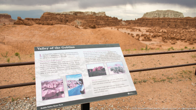 An interpretive sign titled Valley of the Goblins stands before the sandstone formations behind a low rail.