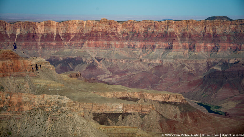 The Colorado River curves at lower right beneath long red and cream canyon walls.