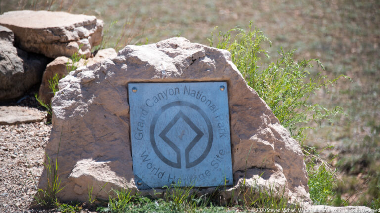 A blue World Heritage Site plaque for Grand Canyon National Park is mounted on a boulder.