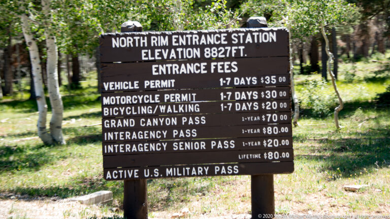 A wooden North Rim entrance board lists permit and pass fees beneath an elevation of 8,827 feet.