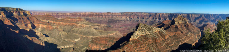 Sunlit canyon walls and shadowed ravines descend through successive plateaus toward a distant horizon.