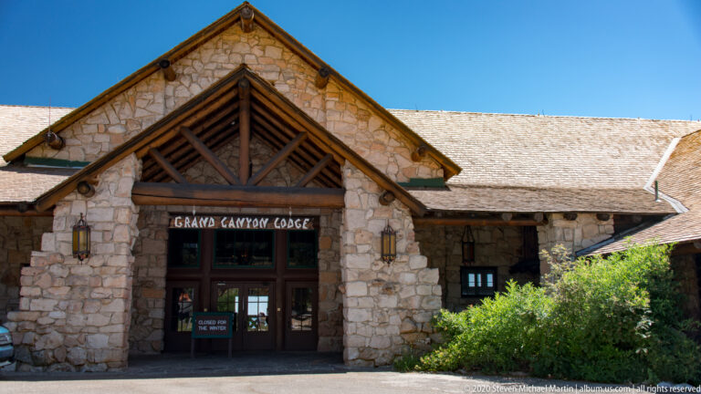 A stone lodge entrance with a timber-trussed gable stands beneath the Grand Canyon Lodge sign.