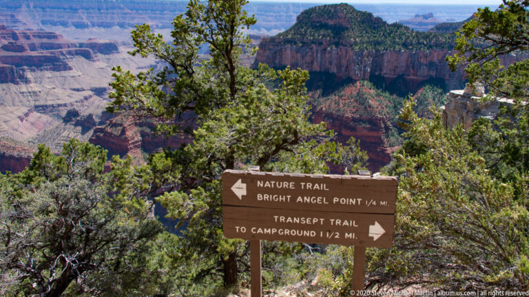 A wooden trail sign points to Bright Angel Point and the Transept Trail above the canyon.