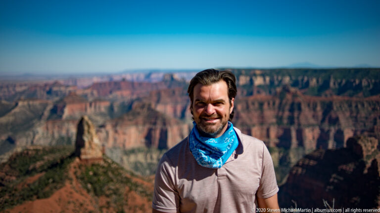 Close portrait of a man in a gray shirt and blue scarf with the canyon blurred behind him.
