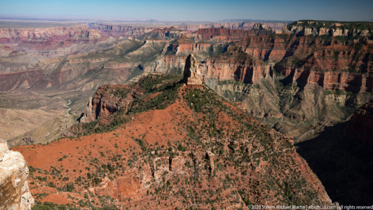 Sunlit red ridge and pale foreground rock overlook a shadowed gorge and distant canyon layers.