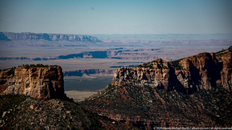 Dark foreground cliffs overlook hazy canyon ridges and a broad distant plateau.