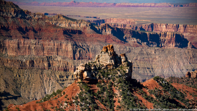 A pale rock butte rises from a red ridge above ravines and layered canyon walls.
