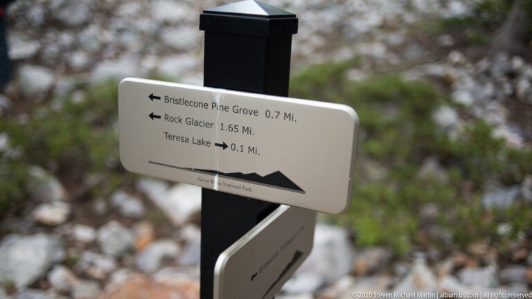 A white trail marker points toward Bristlecone Pine Grove, Rock Glacier, and Teresa Lake with distances.