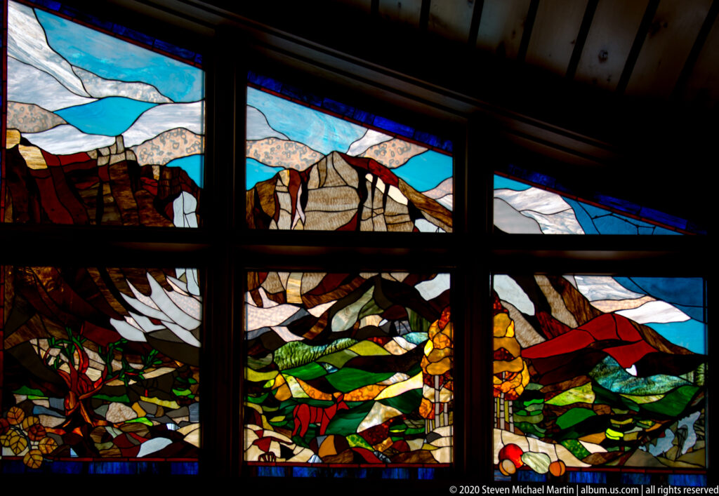 Colorful stained-glass panels depict stylized mountains, wildlife, plants, and landscape bands inside the visitor center.