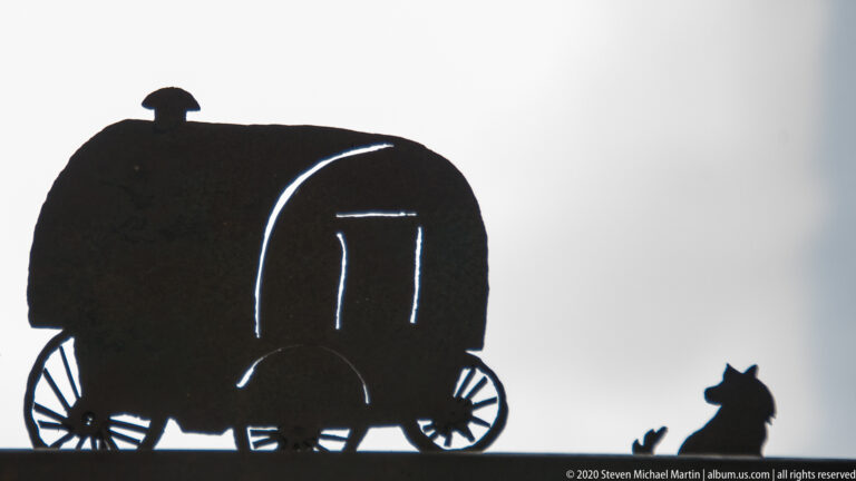 A covered wagon silhouette with spoked wheels stands beside a small animal figure.