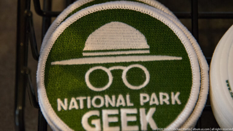 A round green embroidered patch reads “National Park Geek” beneath a simple landscape emblem.