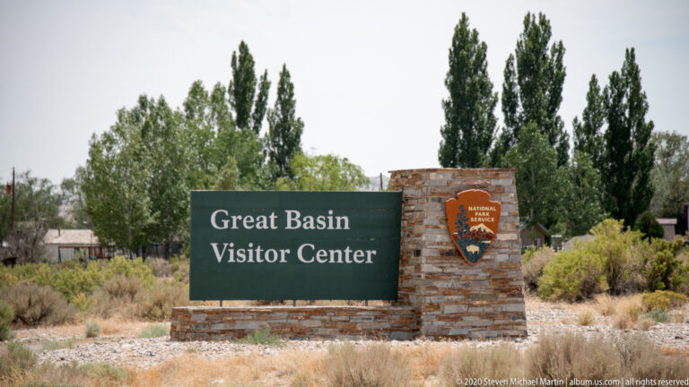 A green Great Basin Visitor Center sign and National Park Service emblem sit on a stone wall.
