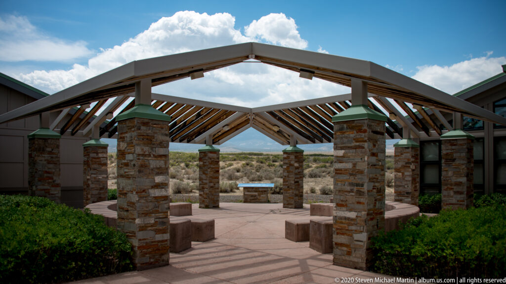A timber canopy shades a paved courtyard lined with stone columns and low benches.