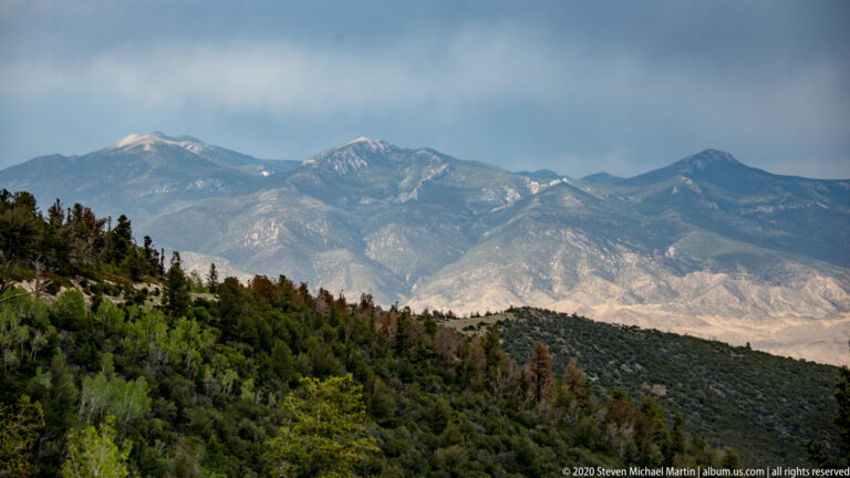 Pale rocky peaks rise above a green forested ridge beneath a hazy sky.