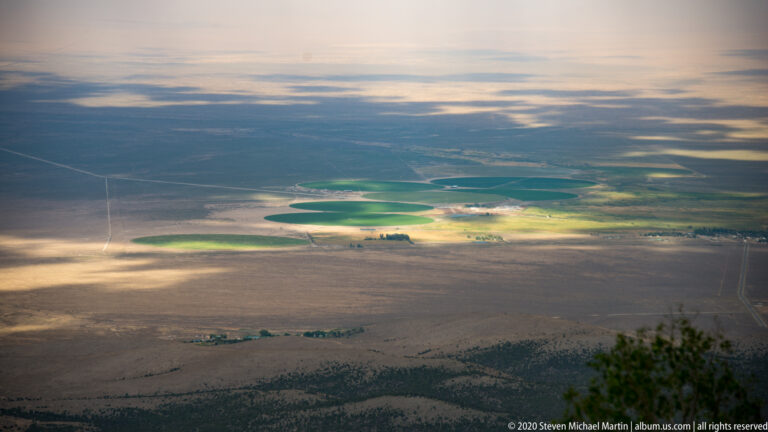 Green agricultural circles and strips punctuate a broad tan basin beneath scattered clouds.