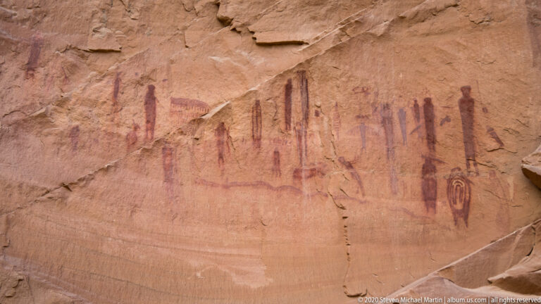 Faded red anthropomorphic figures and motifs span a sandstone wall.