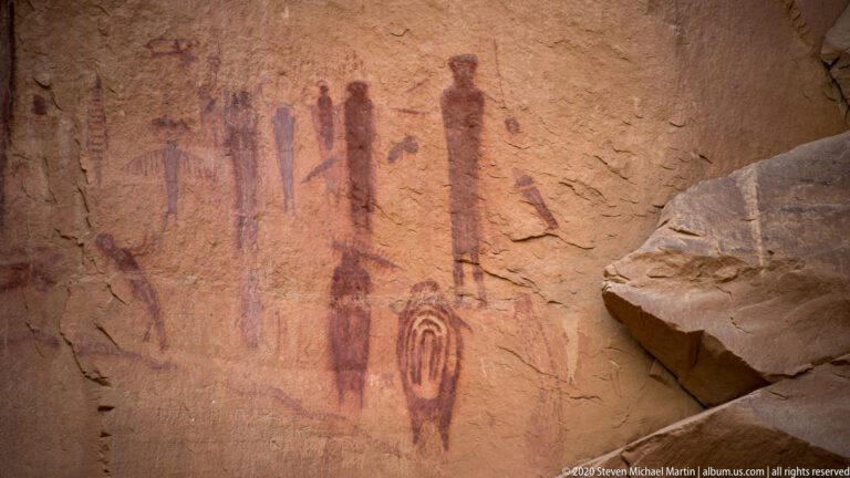 Tall red figures and a nested oval motif appear on a sandstone panel.