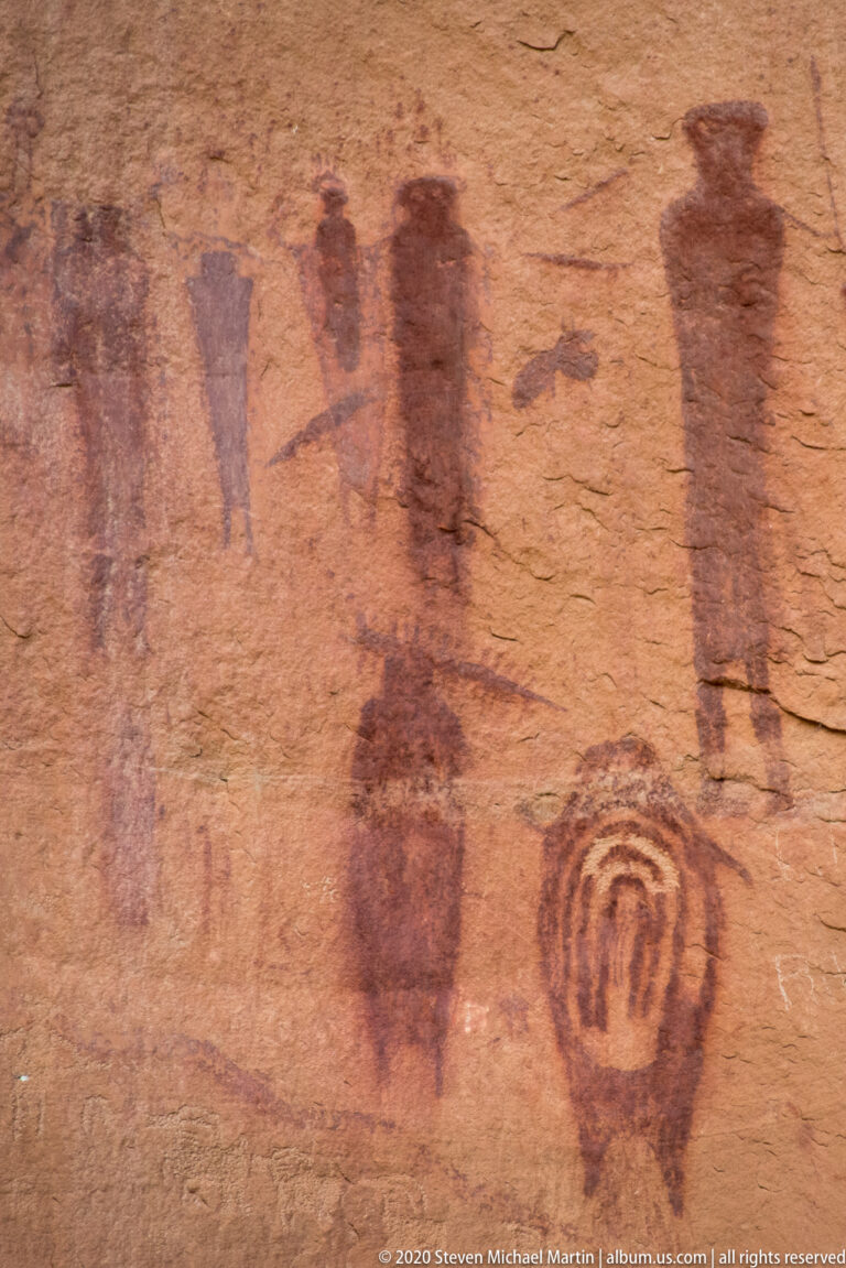 Faded red figures and a concentric oval motif cover a close sandstone surface.