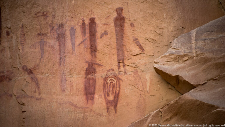 A nested oval motif sits below tall painted figures on a sandstone wall.