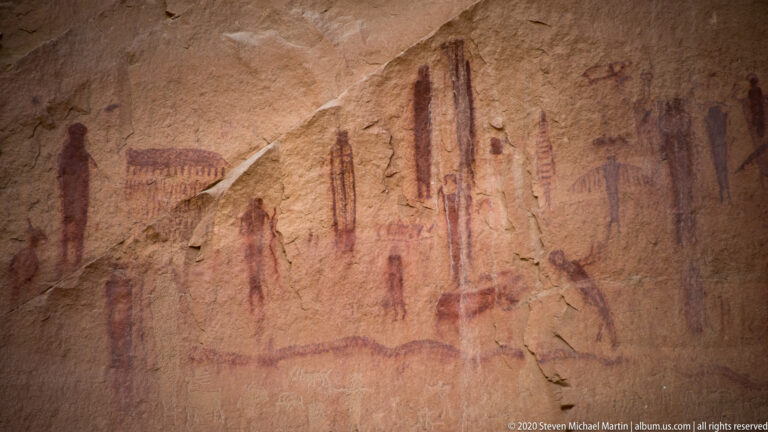 Faded red figures and symbols stretch across a sandstone wall.