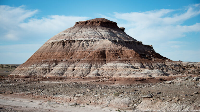 A flat-topped butte shows a dark caprock above fluted pale and rust-colored slopes.