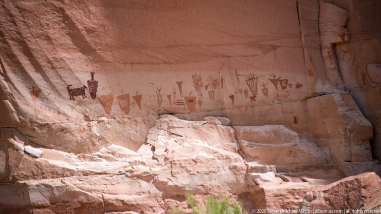 Faded painted figures line a shaded sandstone recess above a broken ledge.