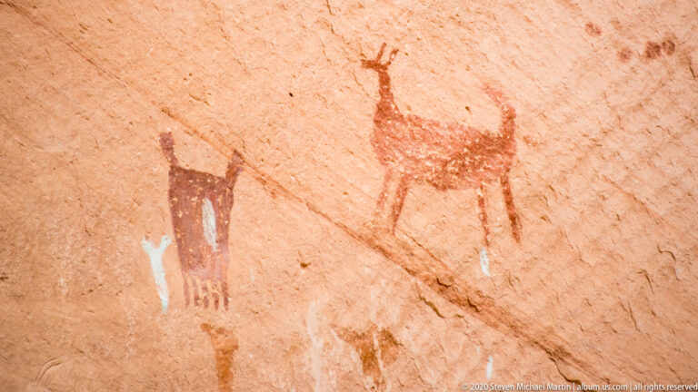 Faded red figures and a horned animal-like form appear on sandstone.