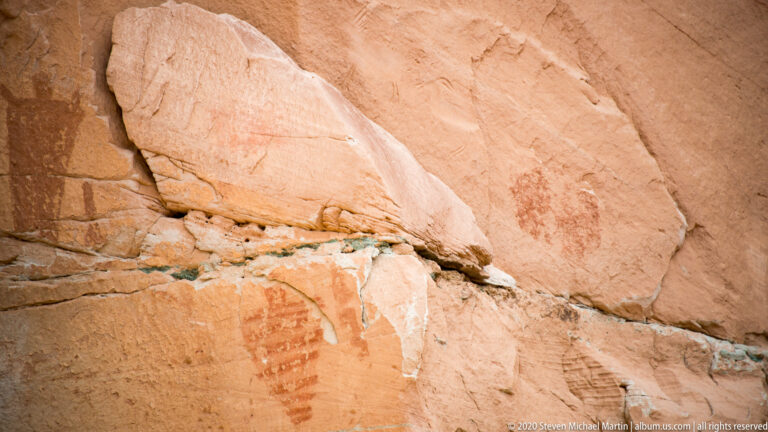 Faint red pictograph marks appear below a diagonal fracture in sandstone.