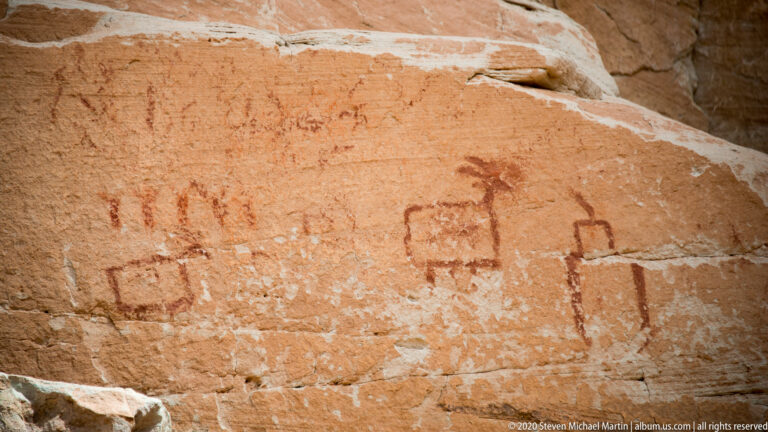 Faded box-shaped animal-like figures and upright marks cross a sloping sandstone panel.