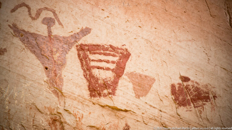 A branching painted form and a striped trapezoid appear on pale sandstone.