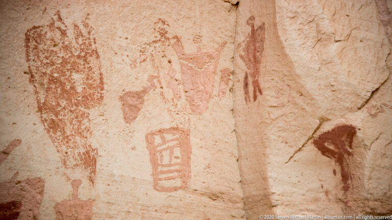 A pale cracked sandstone panel holds a faint central figure, a small barred motif, and darker marks at right.
