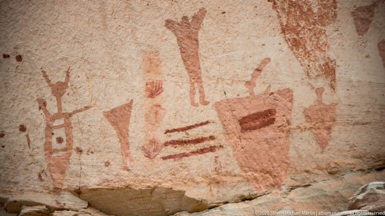 A broad sandstone panel displays red geometric motifs, parallel bars, and elongated human-like forms.