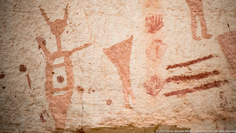 A pale outlined rectangle, muted red triangle, and three horizontal bars are painted on sandstone.