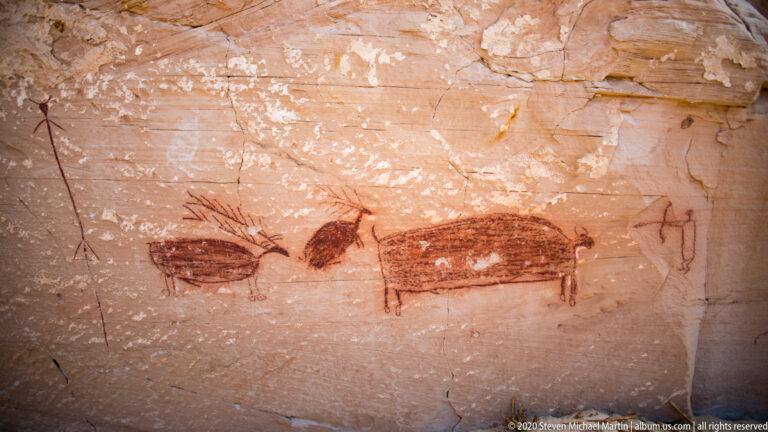 A small dark stick figure with outstretched arms is painted on horizontally striated sandstone.