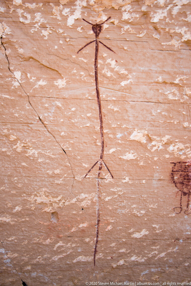 A large rounded quadruped and smaller painted figures form a group along a shaded sandstone ledge.