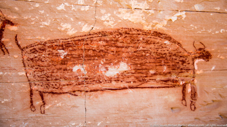 A large reddish quadruped with parallel body stripes is painted across horizontal sandstone.