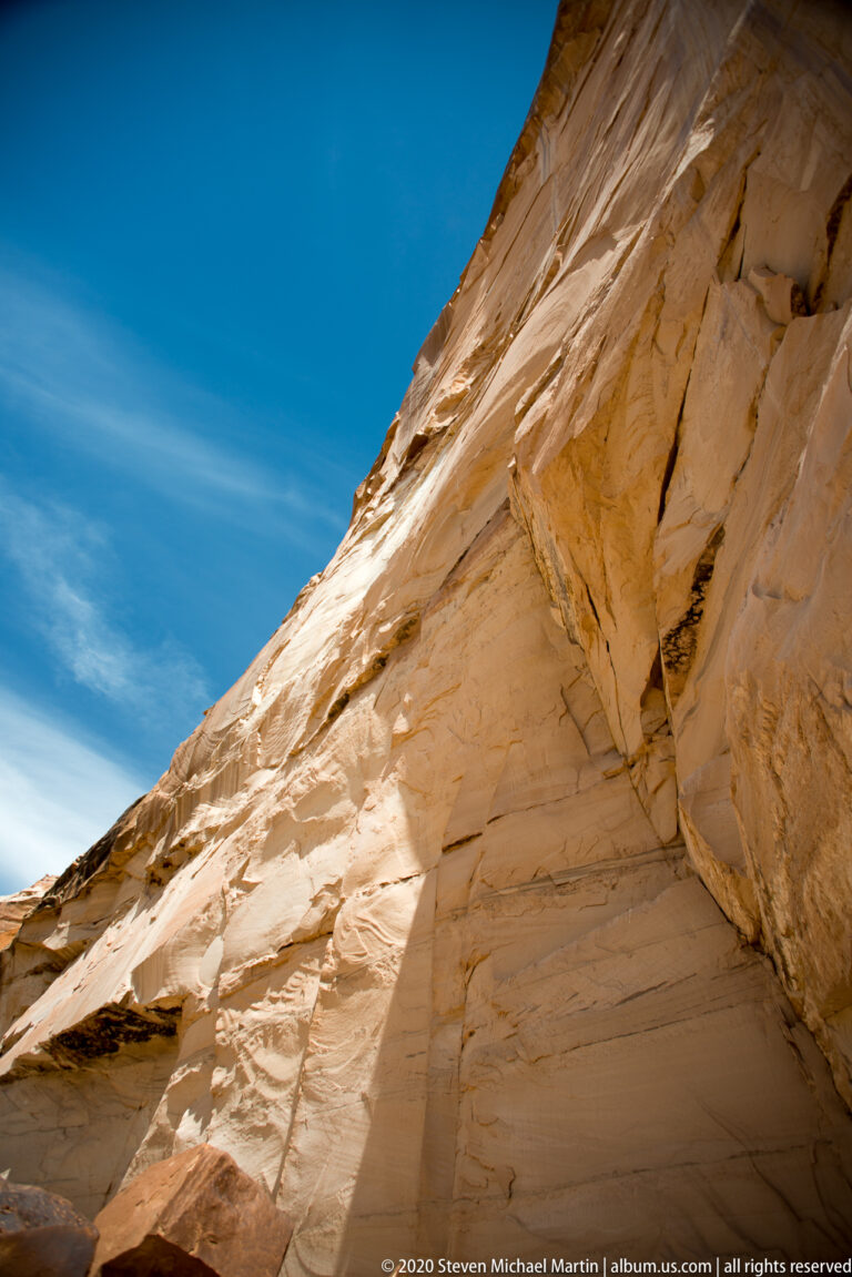 A curved orange sandstone wall rises diagonally beneath a clear blue sky.