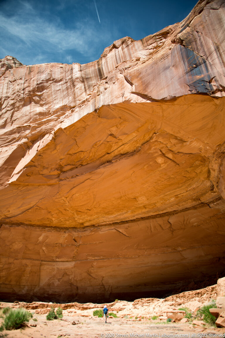 Faded painted figures and large pale modern-looking inscriptions overlap on a dark sandstone wall.