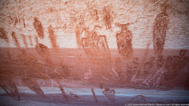 A large reddish oval outline with a pale center sits above a dark band on sandstone.