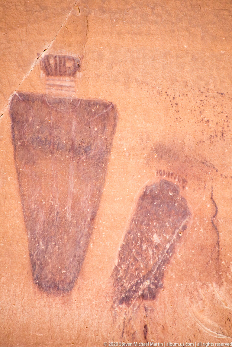 Two dark tapered forms appear on orange sandstone, with faint marks above and beside them.