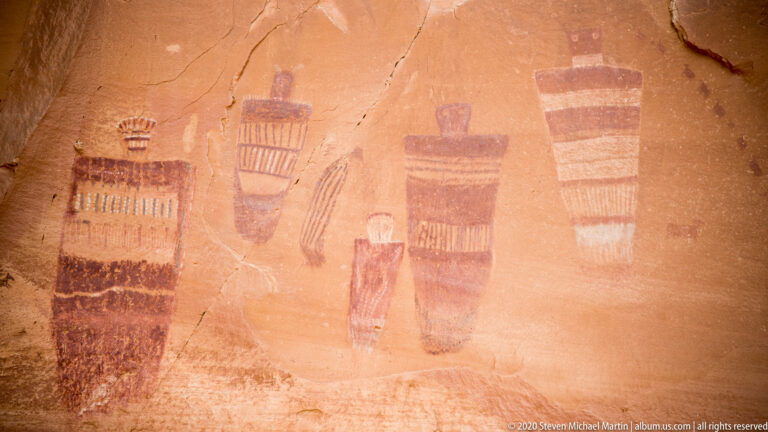 Several tall painted forms with striped and banded interiors surround a narrow central figure.